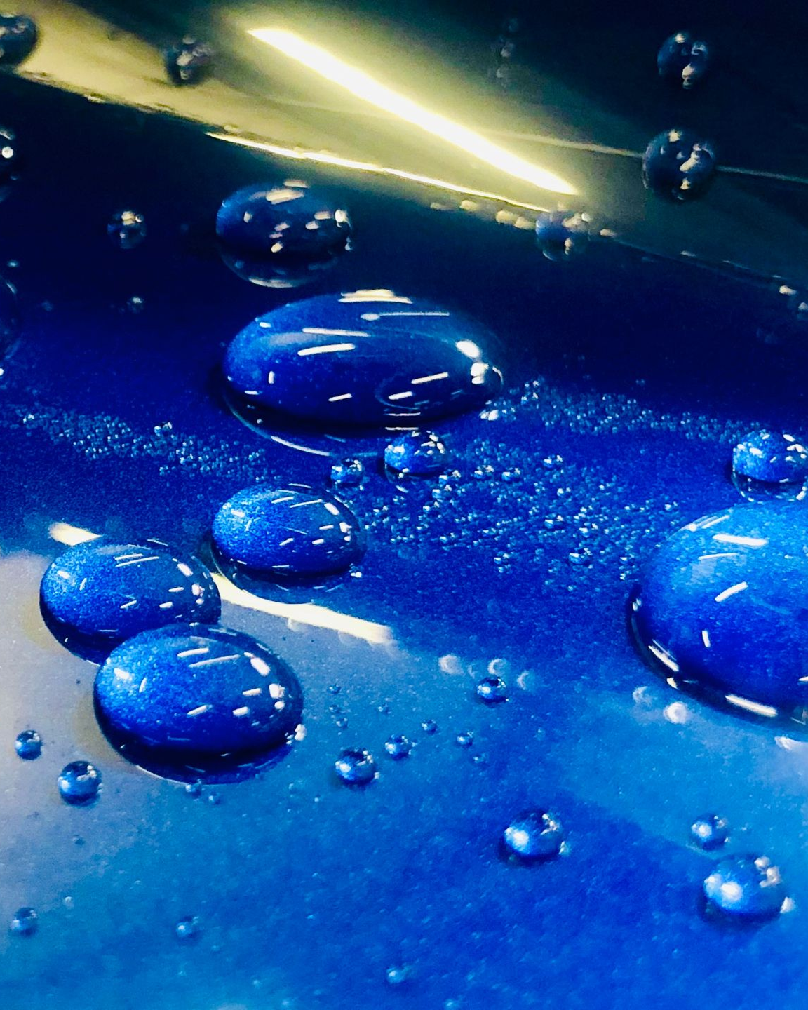 Blue water droplets on a glossy blue surface with sparkling highlights