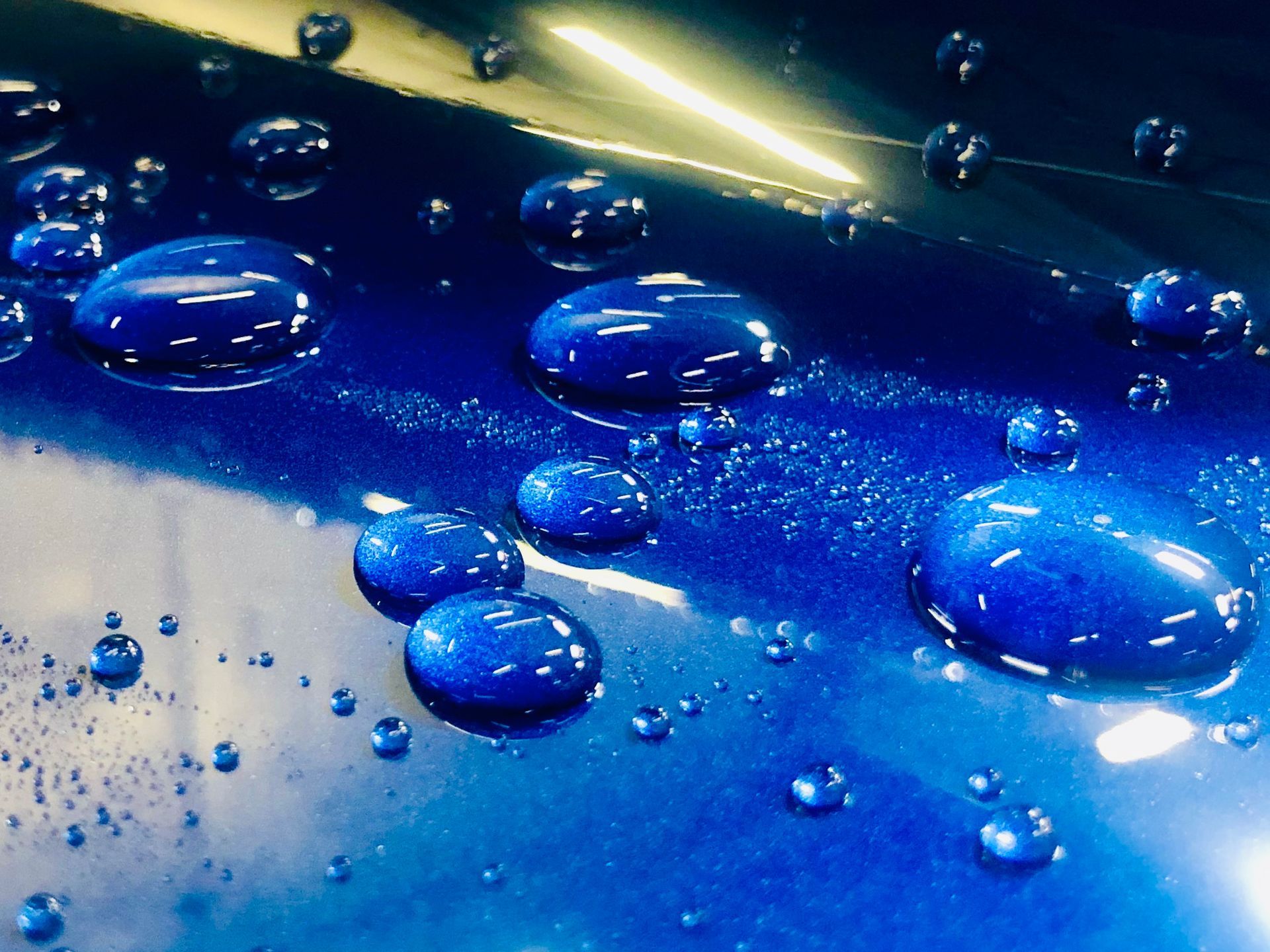Close-up of clear water droplets beading on a vibrant, glossy blue surface.