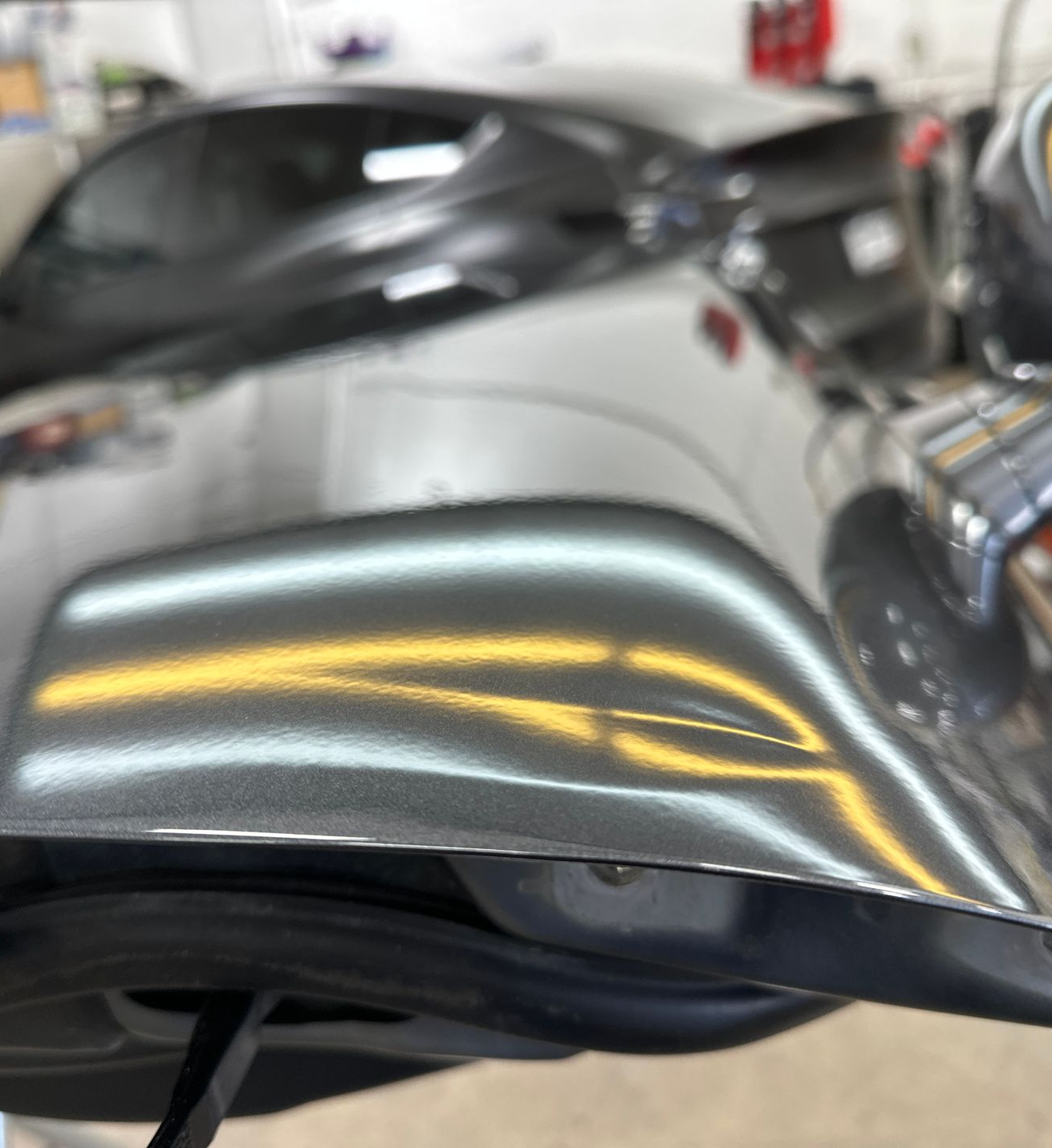 A technician uses a specialized metal tool to perform paintless dent repair on the roof of a dark car.