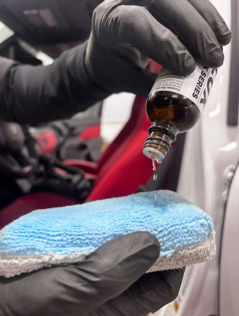 A person is polishing the hood of a blue car.