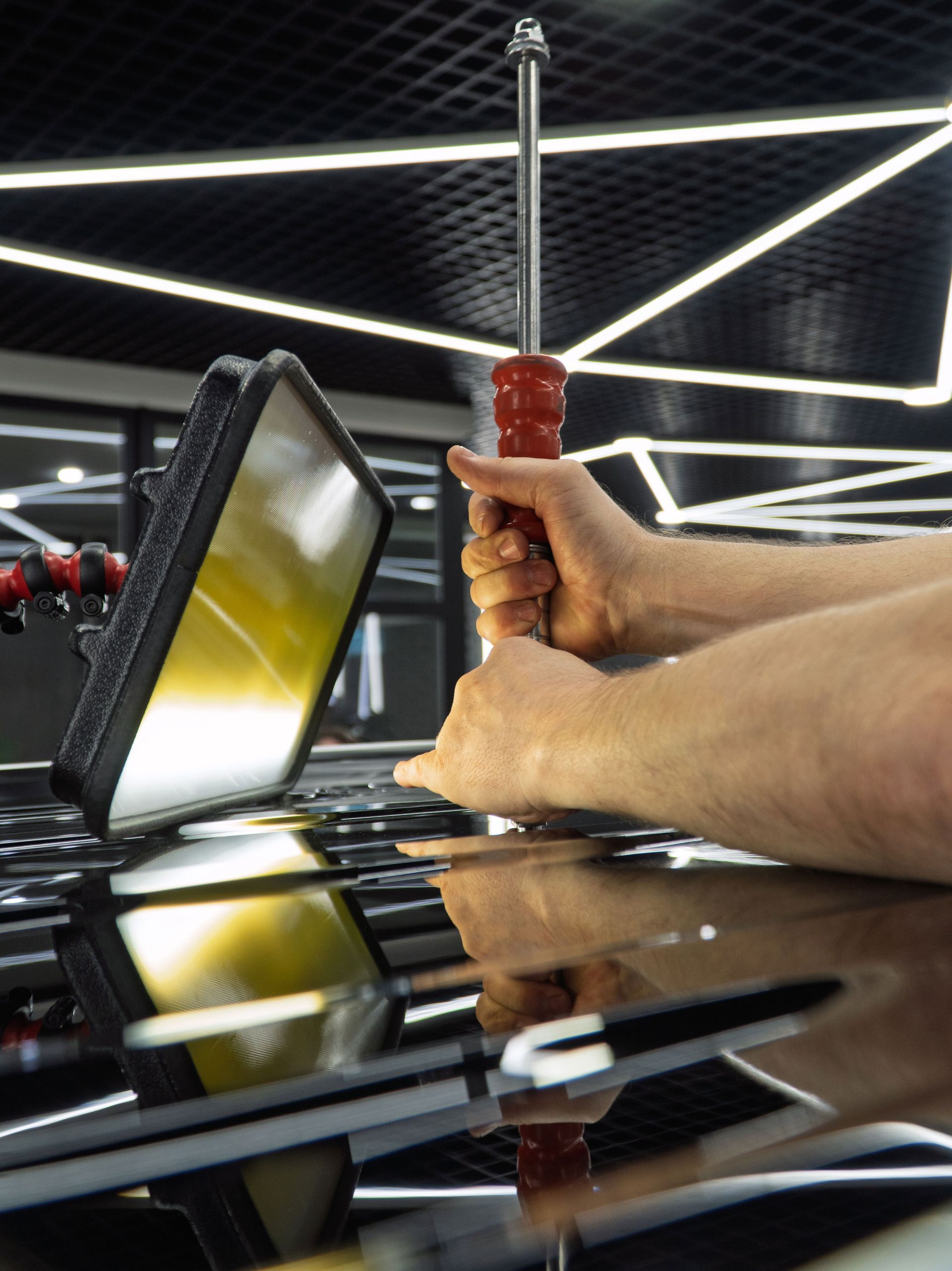 A technician uses a rod tool and a specialized reflection light to perform paintless dent repair on a car’s hood.