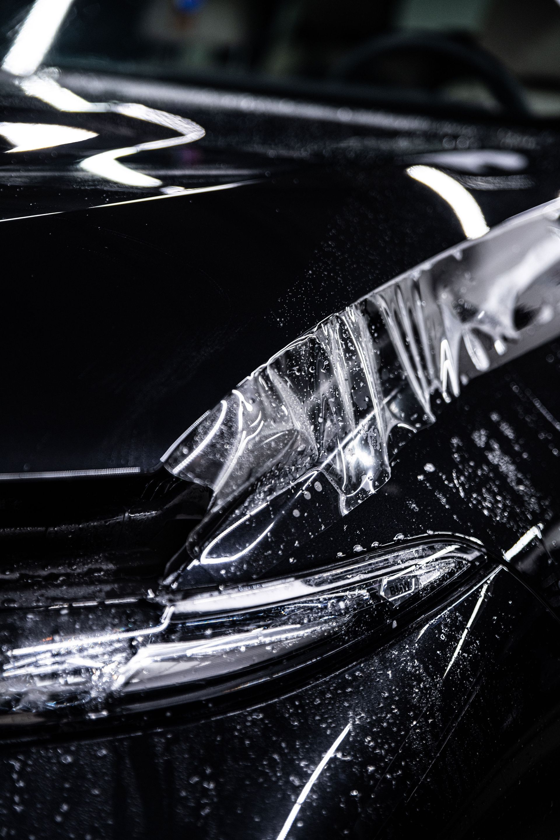 A clear protective film is being applied to the glossy black hood and headlight of a vehicle.