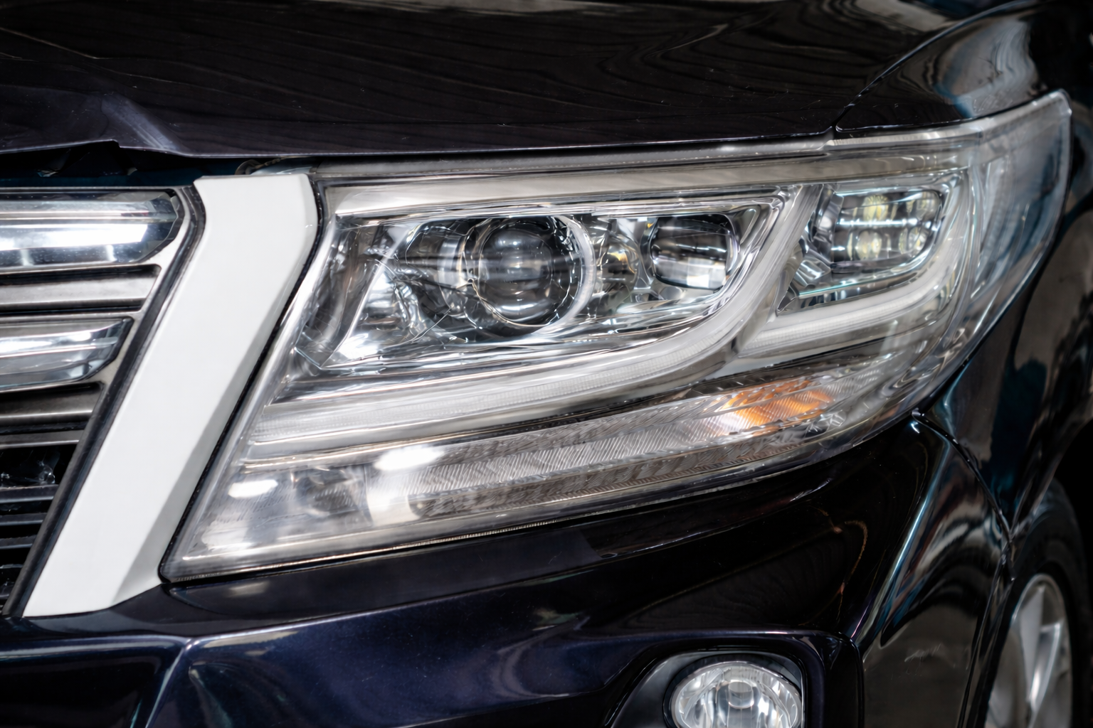 Close-up of a black car’s front headlight and chrome grille detail