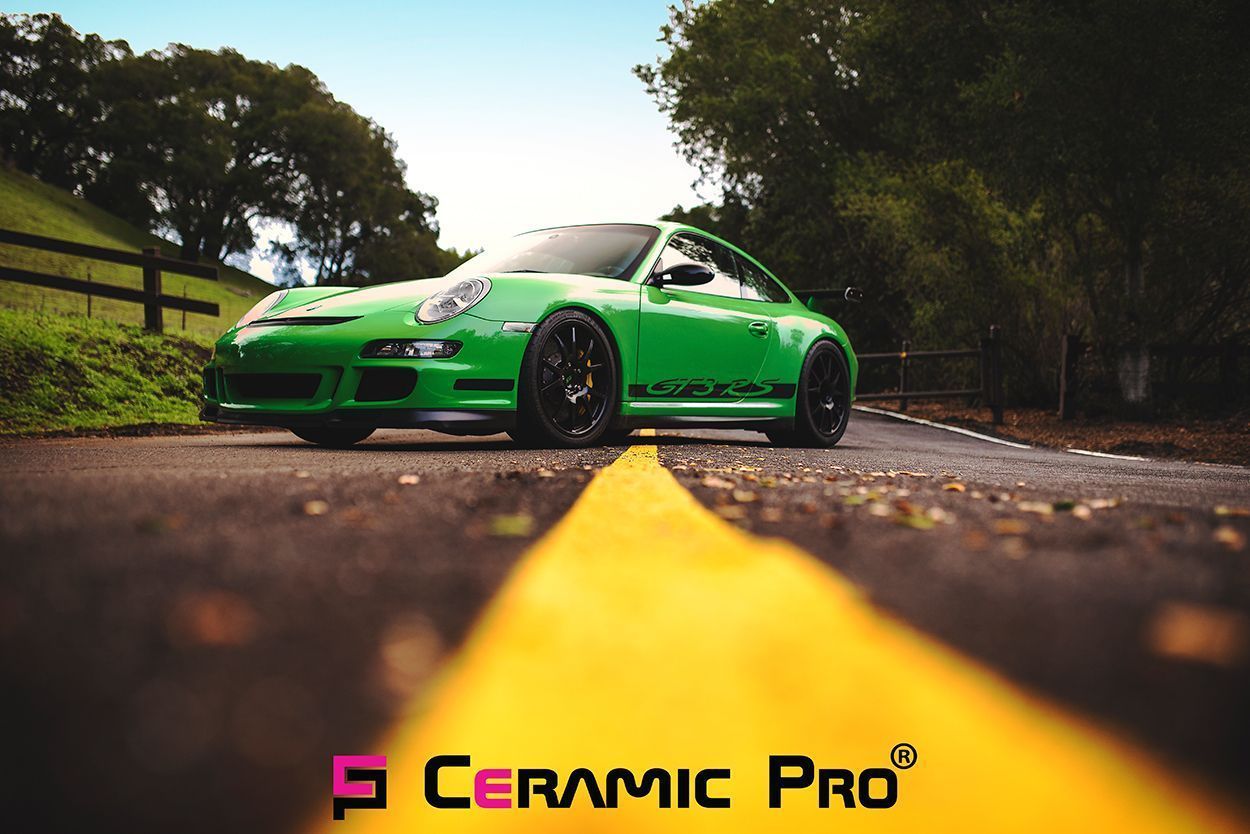 A lime green Porsche 911 GT3 sits on a quiet country road with a yellow center line and forest backdrop.
