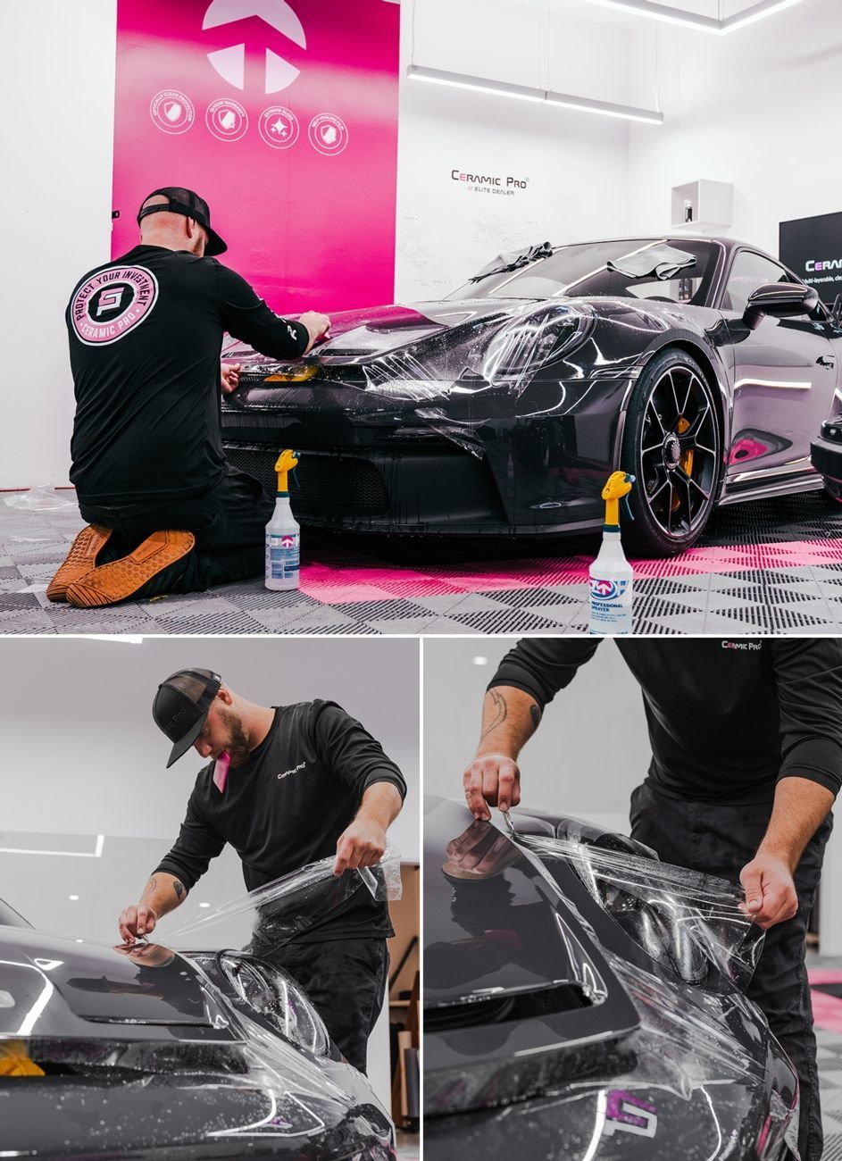 A technician in a black uniform applies clear protective film to the hood of a black luxury car in a professional shop.