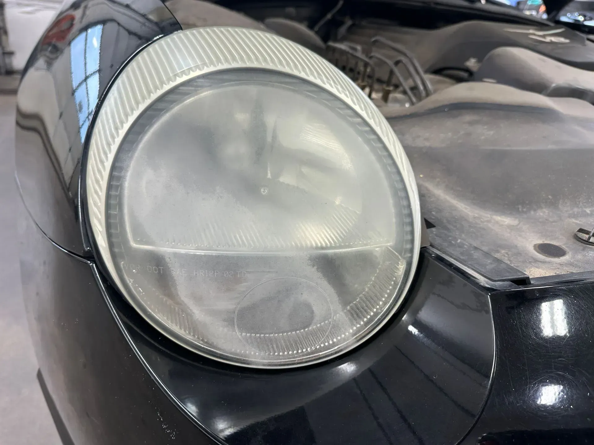 A close-up view of a dusty, round car headlight on the front of a black vehicle.