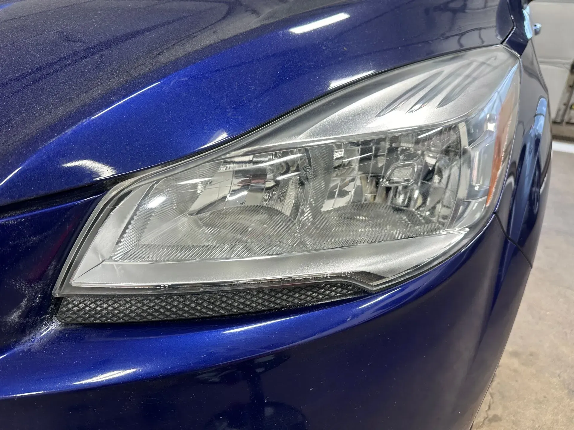 Close-up of a blue car's headlight assembly, showing the clear lens, internal reflectors, and surrounding body paint.