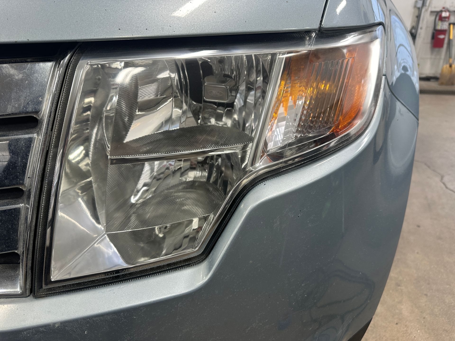 Close-up of a gray car's front headlight assembly featuring a clear lens, a chrome reflector, and an amber turn signal.