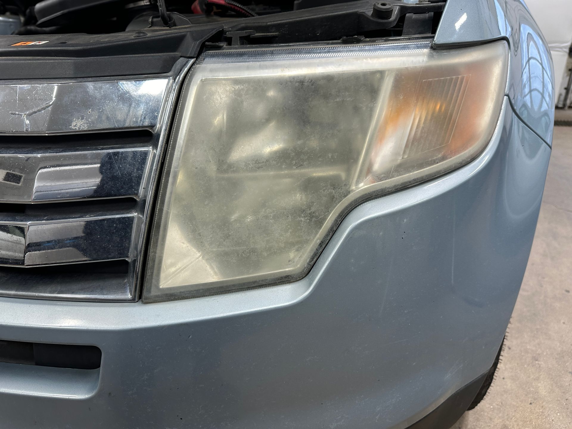 A close-up view of a faded, yellowish headlight lens on the front corner of a silver vehicle.