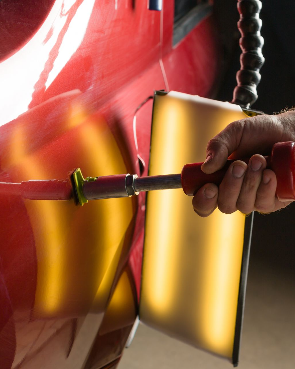 A dent repair tool with a reflection board positioned over a crease on the silver door panel of a car.