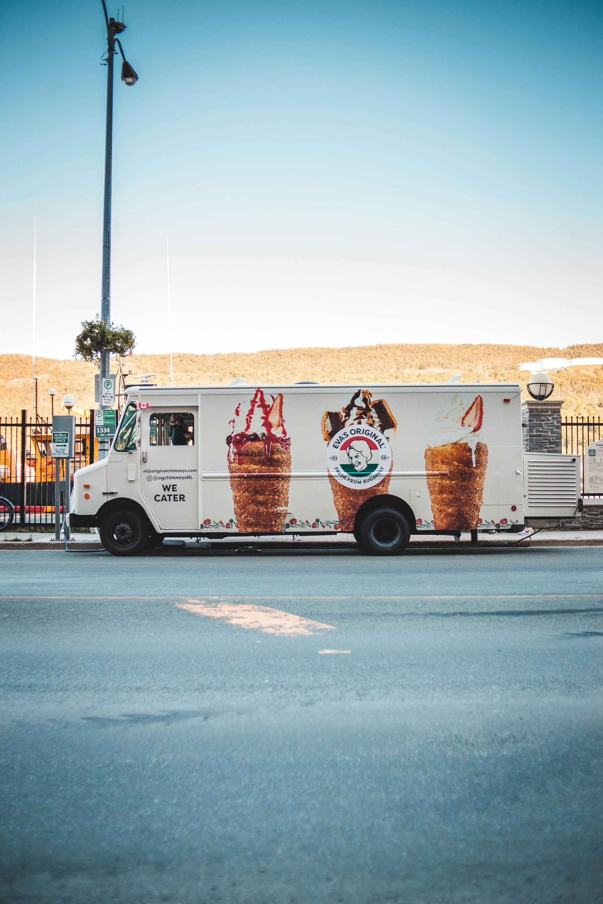 A white ice cream truck with graphics of three ice cream cones parked on a street under a clear blue sky.