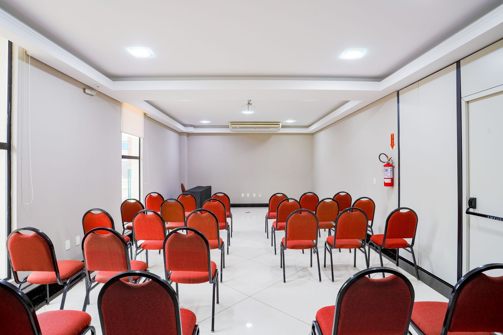 Sala de conferências vazia com fileiras de cadeiras vermelhas voltadas para a tela frontal.