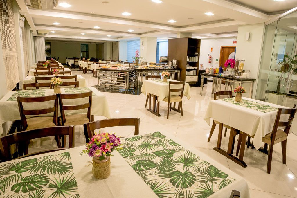 Salão de banquetes espaçoso com mesas impecavelmente arrumadas, toalhas de mesa brancas e arranjos florais sob iluminação aconchegante.