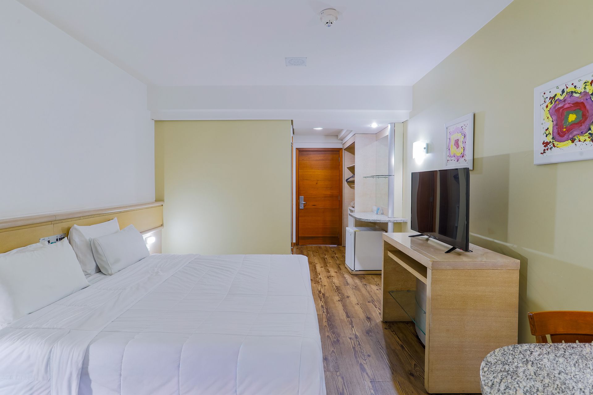 Quarto de hotel impecável com cama grande, TV, cômoda e porta para o banheiro.