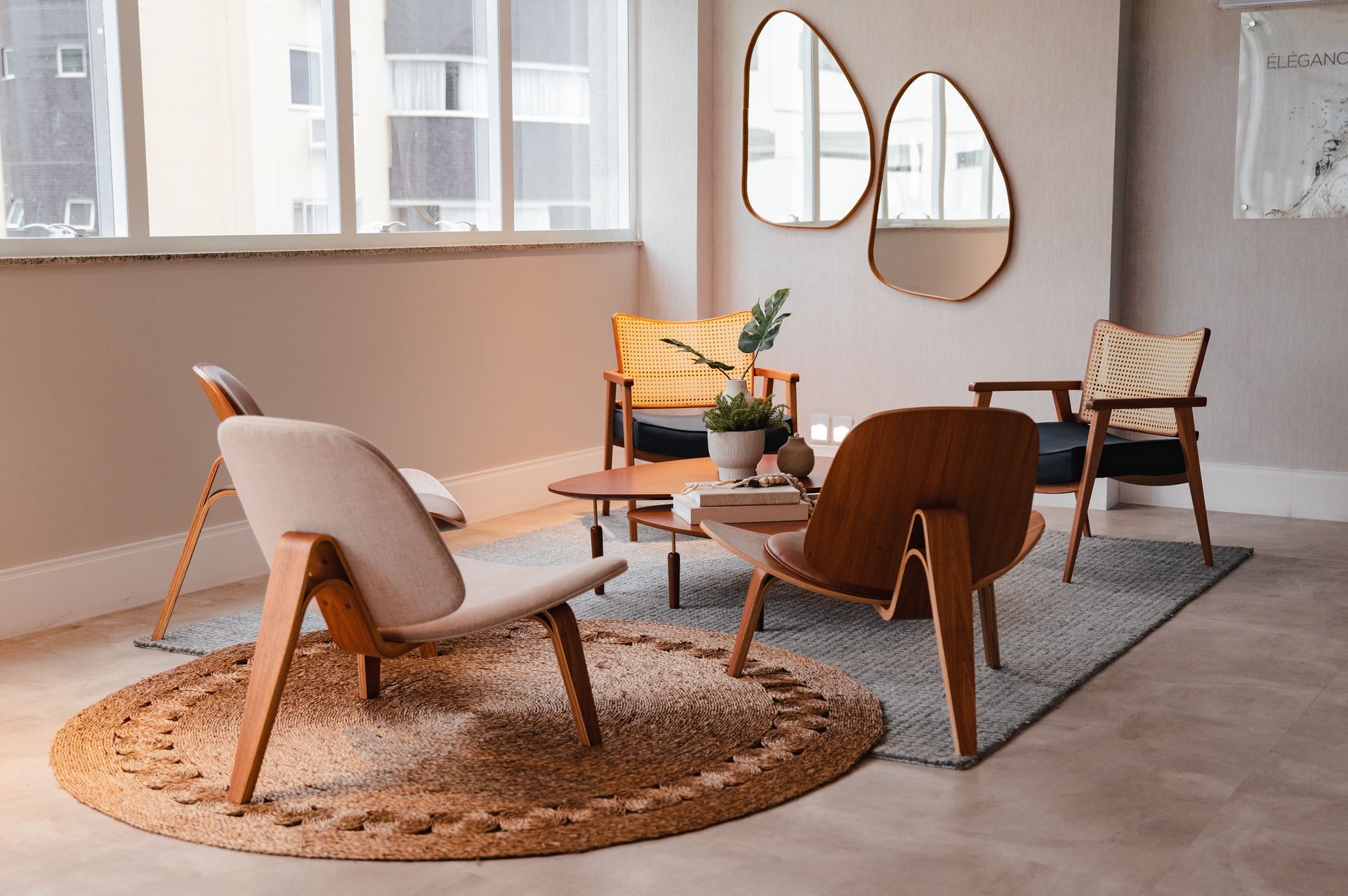 Sala de estar moderna e aconchegante com cadeiras em tons neutros, tapete redondo e mesa de centro de madeira junto a grandes janelas.