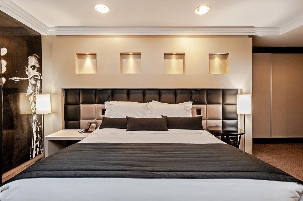 Quarto de hotel moderno com cama king-size, cabeceira estofada, iluminação embutida aconchegante e decoração neutra.