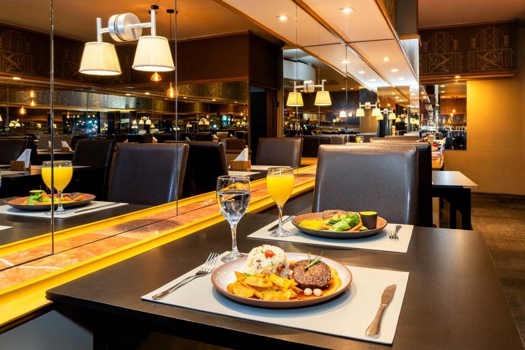 Conjunto de mesa de jantar moderno para restaurante, com pratos servidos, taças de vinho e iluminação ambiente aconchegante.