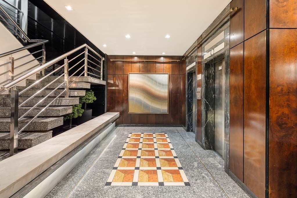 Hall de entrada moderno com escadas, elevador e passarela de ladrilhos estampados sob iluminação aconchegante.