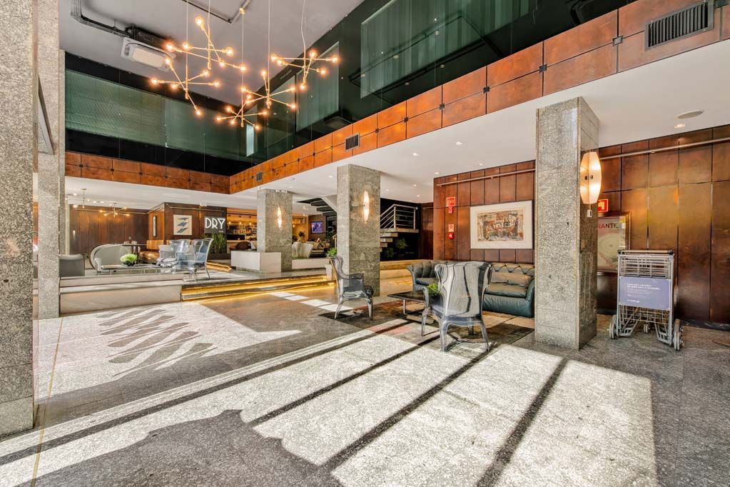 Hall de entrada moderno do hotel com colunas de pedra, iluminação aconchegante e área de estar sob um pé-direito alto.