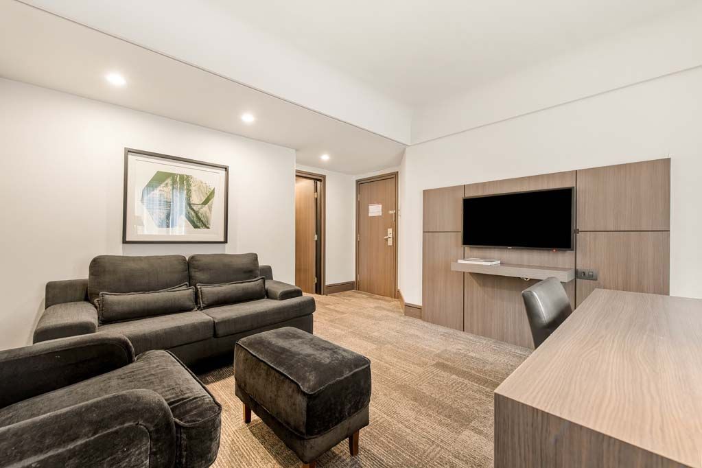 Sala de estar moderna com sofás cinza, pufes, TV de parede e uma escrivaninha sob iluminação aconchegante.