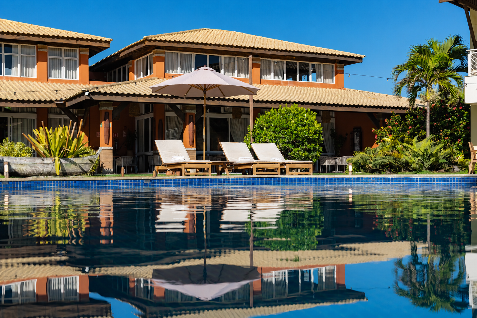 Villa de luxo com espreguiçadeiras à beira da piscina e palmeiras refletidas nas águas calmas.