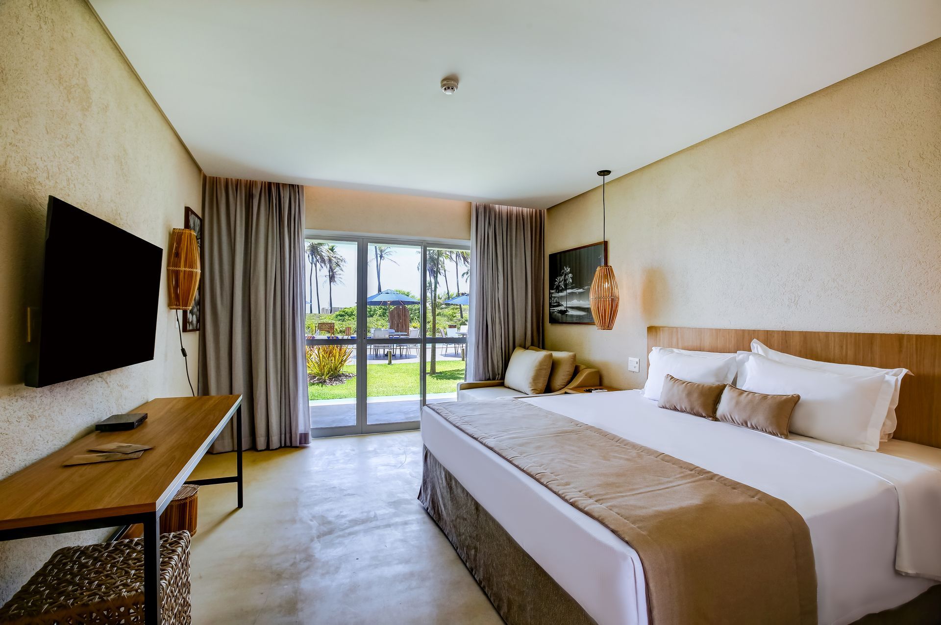 Quarto de hotel moderno com duas camas, TV de parede, escrivaninha e portas de vidro deslizantes para uma varanda ou pátio.