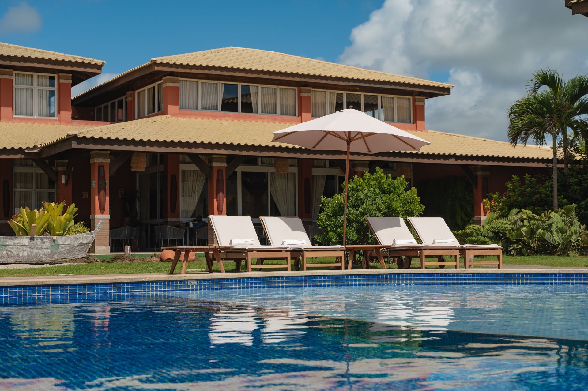 Villa de luxo com piscina, espreguiçadeiras e guarda-sol branco sob um céu azul.