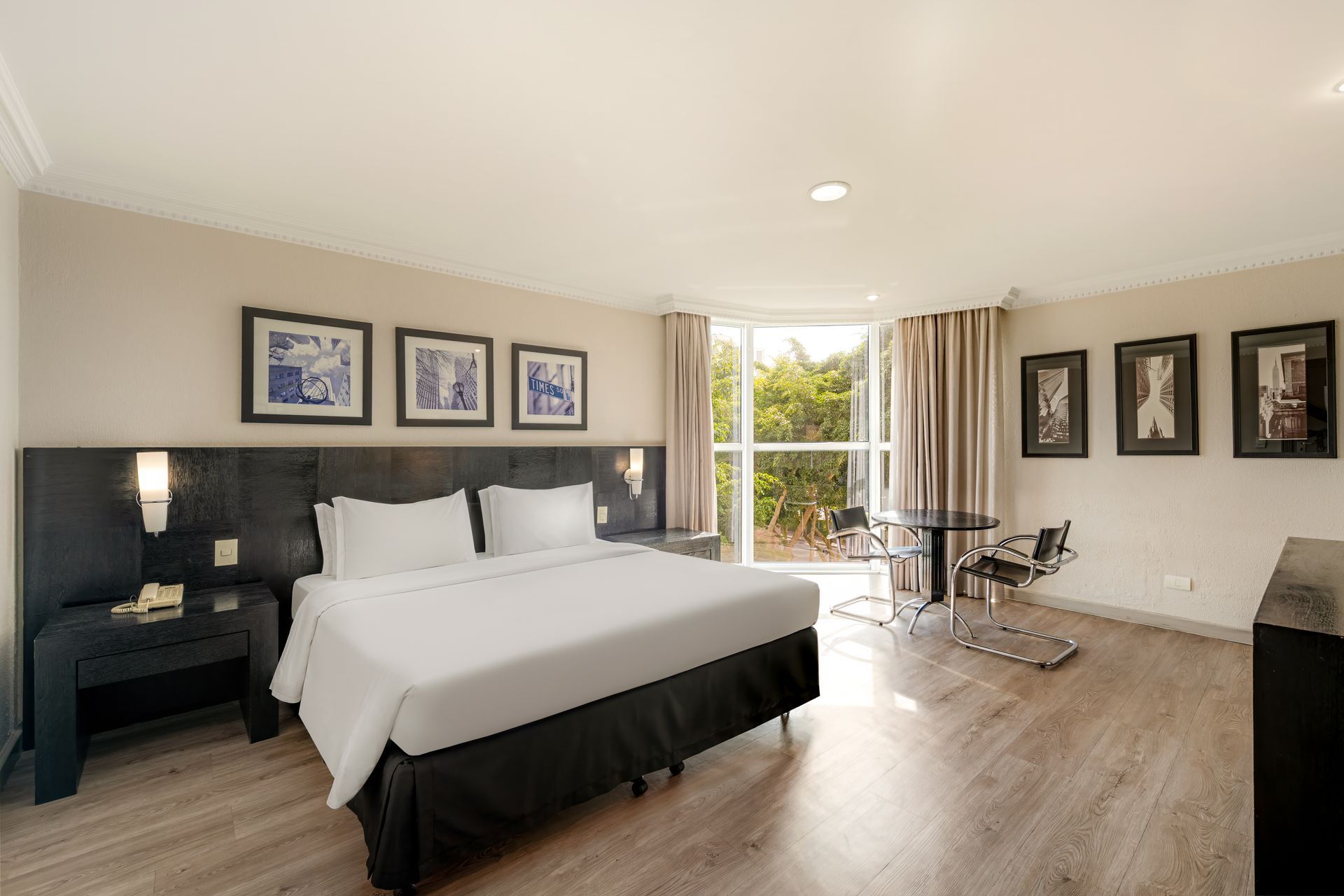 Quarto de hotel moderno com cama king-size, obras de arte emolduradas e portas de varanda com vista para o exterior.