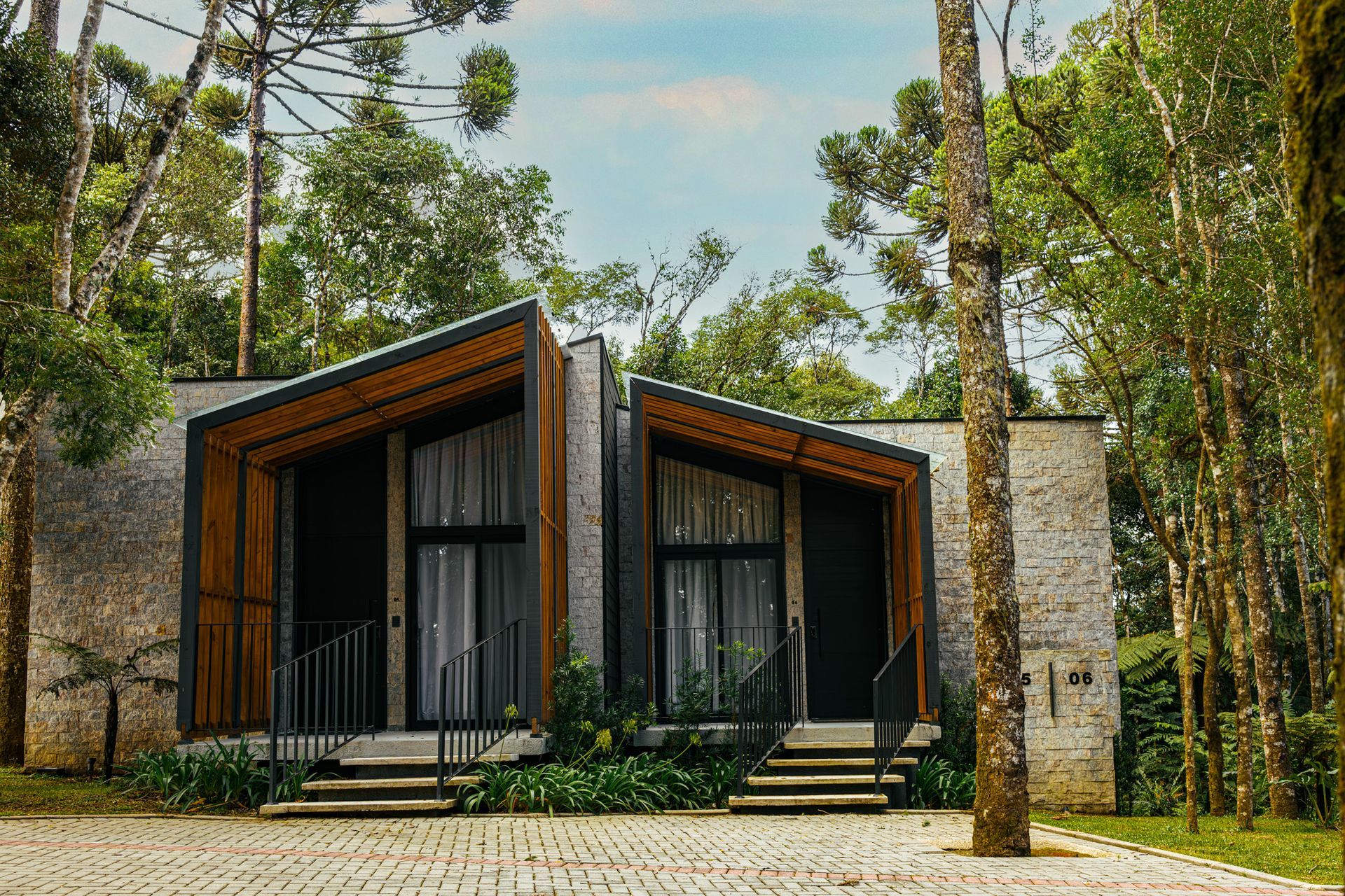 Cabana moderna com fachadas de madeira escura e detalhes em pedra, aninhada entre árvores altas em uma clareira na floresta.