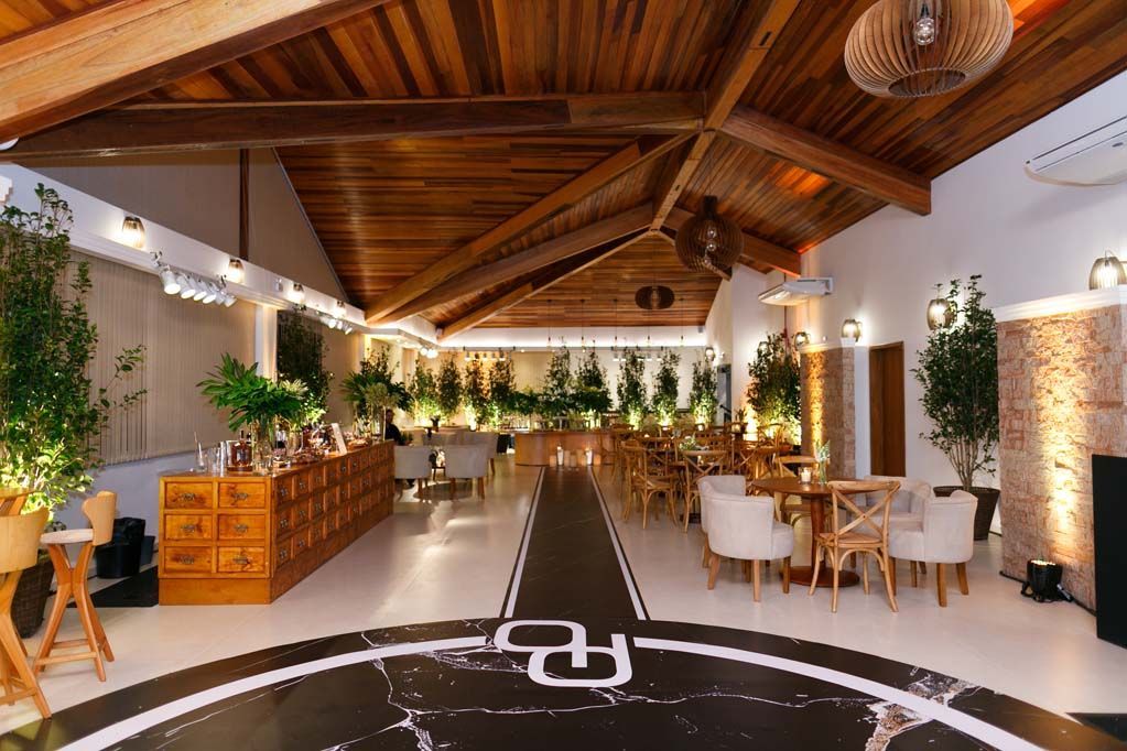 Elegante salão de eventos interno com teto abobadado de madeira, plantas, mesas e iluminação aconchegante.