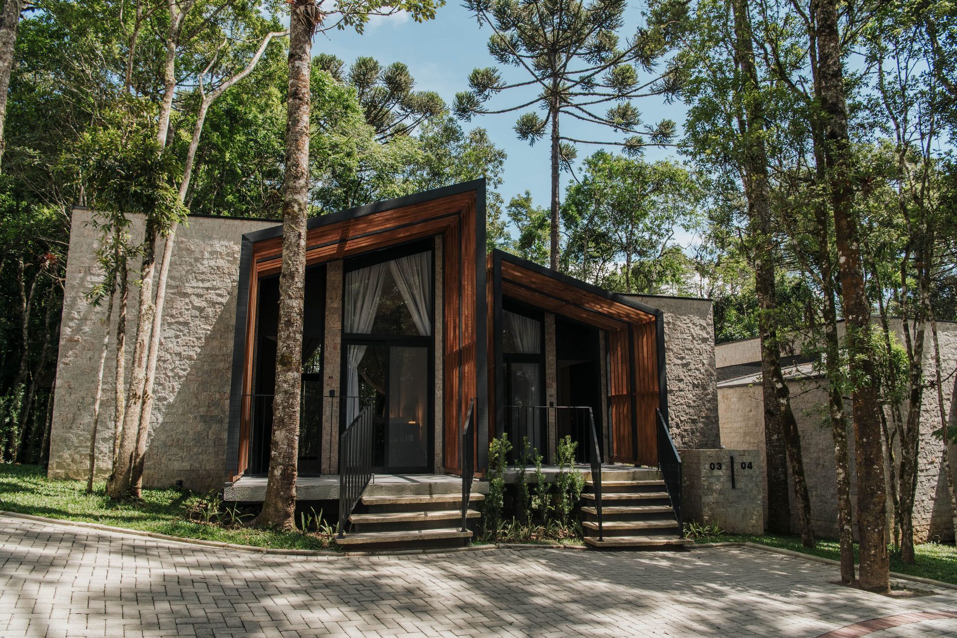Cabana moderna com fachada de madeira e pedra em meio a árvores altas.