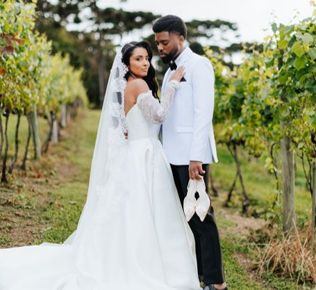 Casal em trajes de casamento brancos, juntos em um jardim de vinhedo.