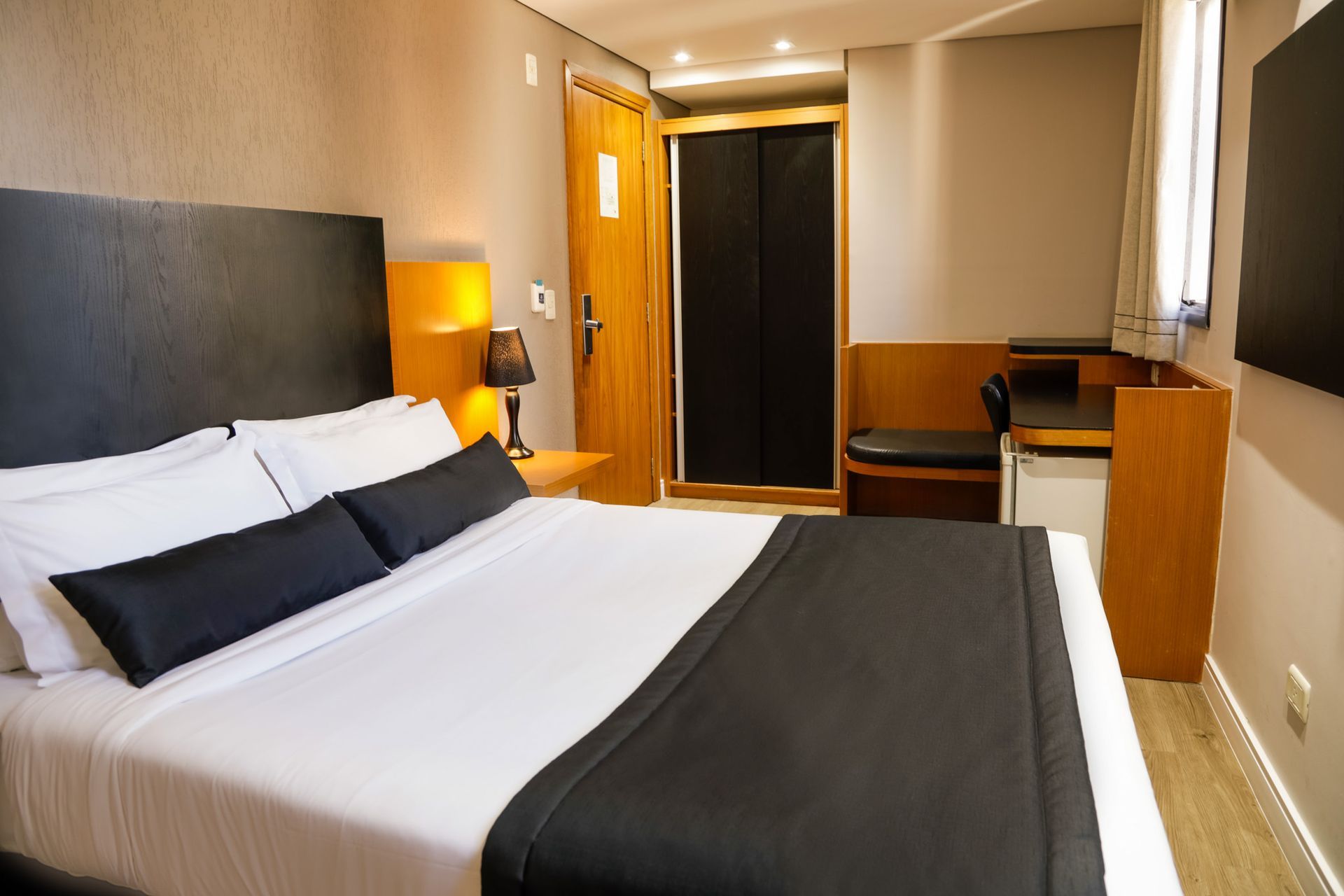 Quarto de hotel moderno com cama arrumada, escrivaninha e mobiliário aconchegante em madeira.