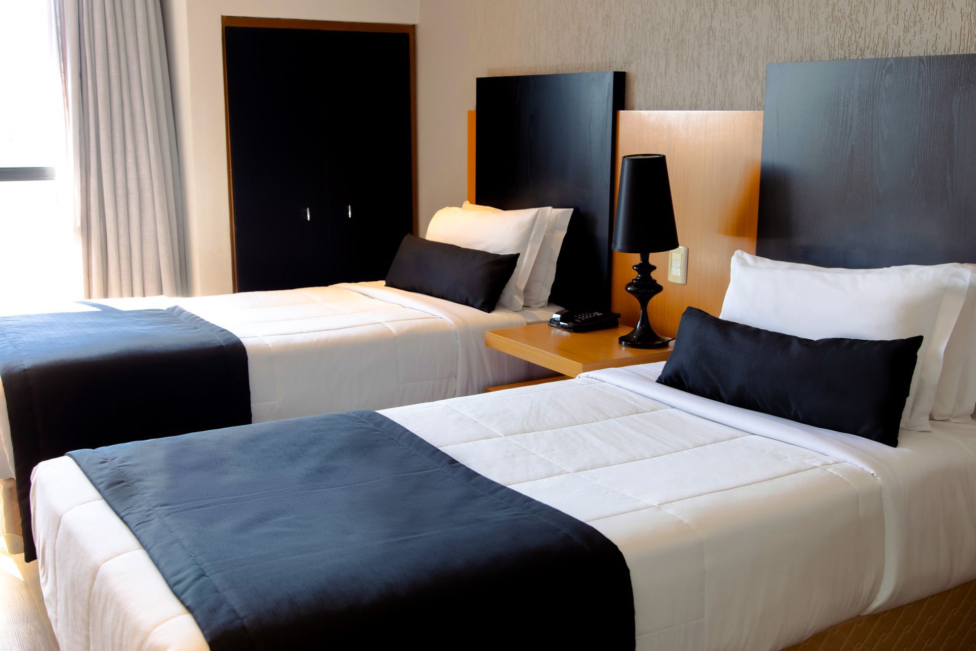 Duas camas de solteiro bem arrumadas em um quarto de hotel moderno com detalhes escuros e um abajur.