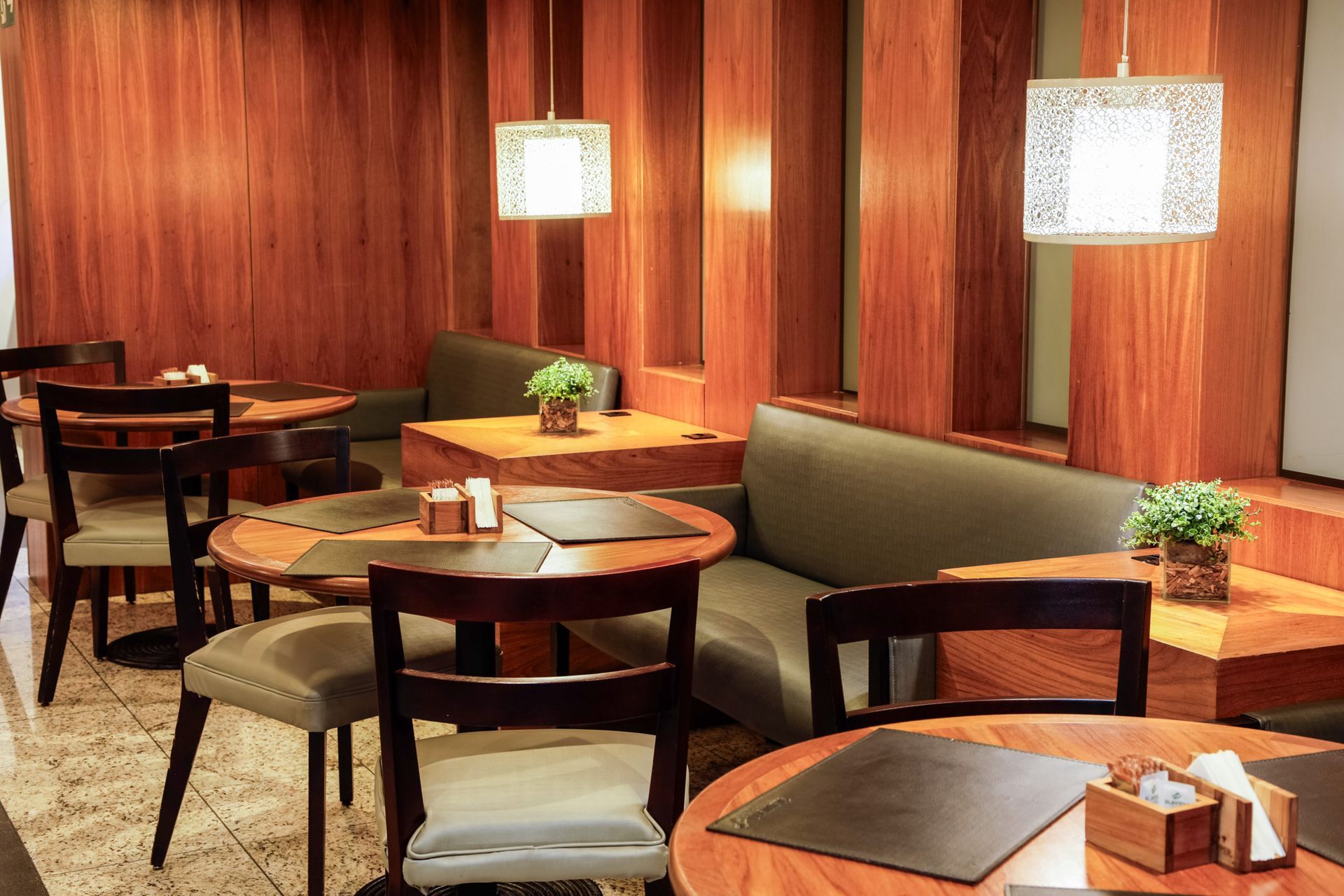 Área de jantar aconchegante do restaurante com paredes de madeira, mesas redondas e cabines com almofadas.