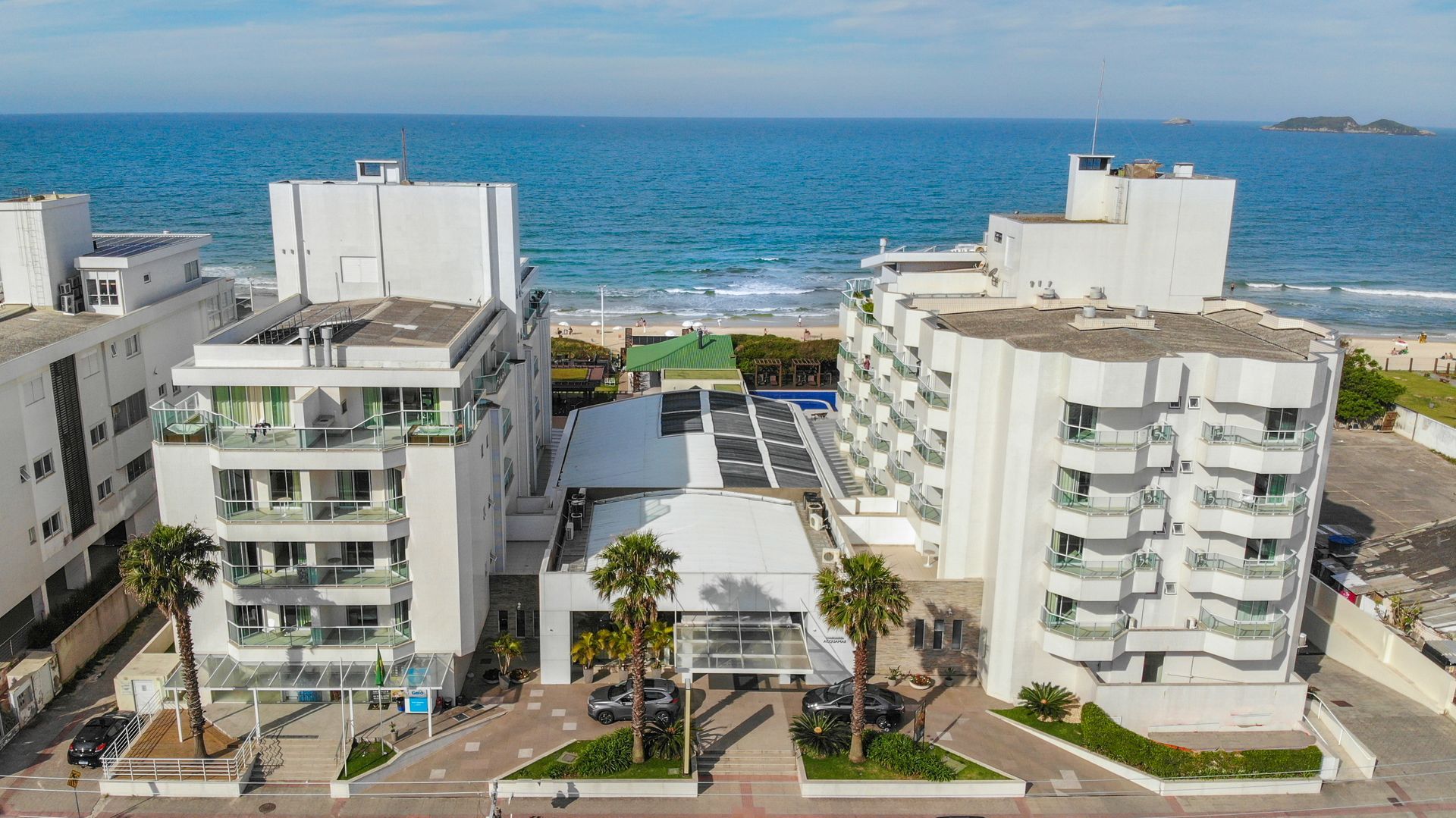 Prédios de apartamentos modernos à beira-mar com vista para o oceano sob um céu claro.