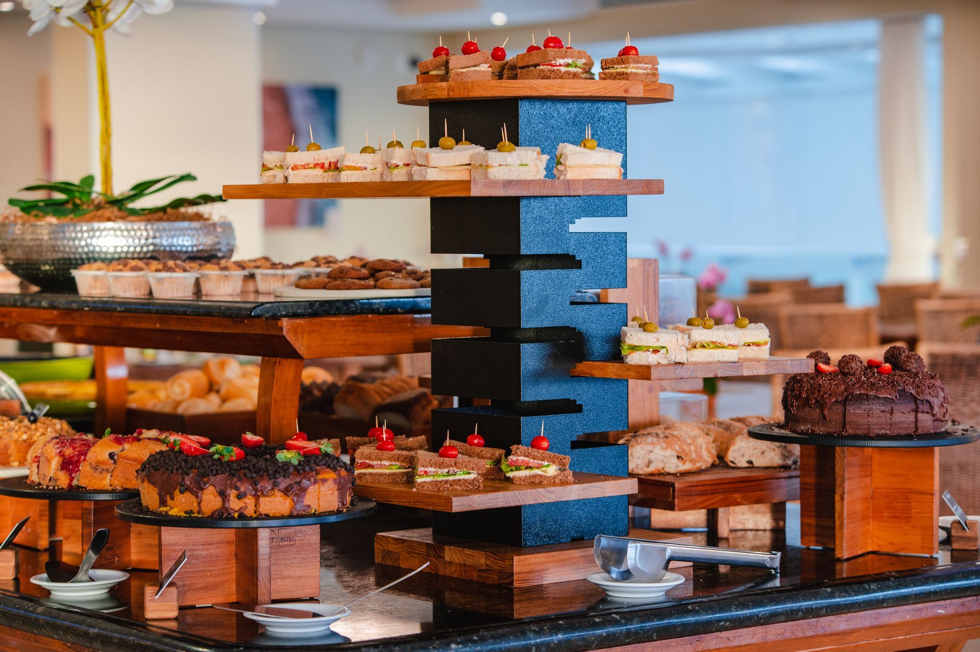 Buffet de sobremesas com doces e frutas em bandejas de vários andares em uma sala de jantar iluminada.