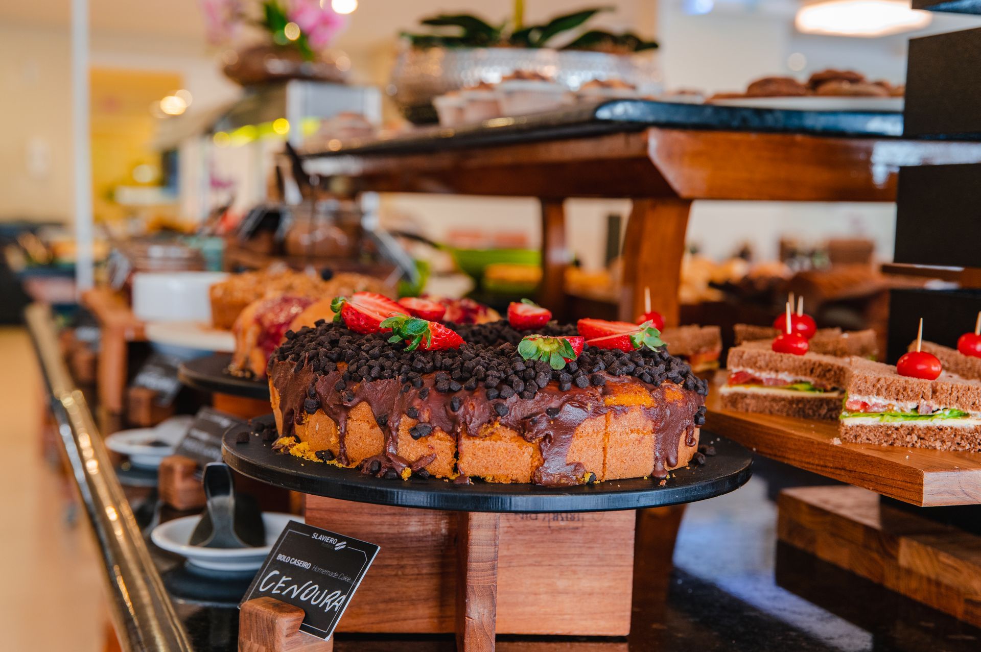 Exposição de sobremesas com um bolo de chocolate coberto com morangos em um balcão de café.