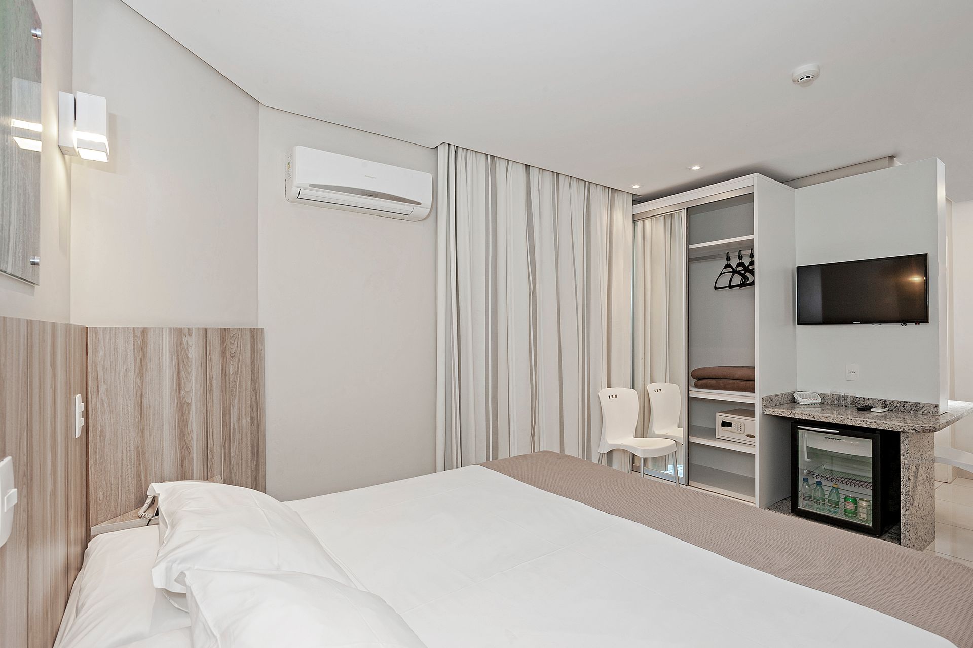 Quarto de hotel moderno com duas camas, TV de parede, escrivaninha e cortinas.