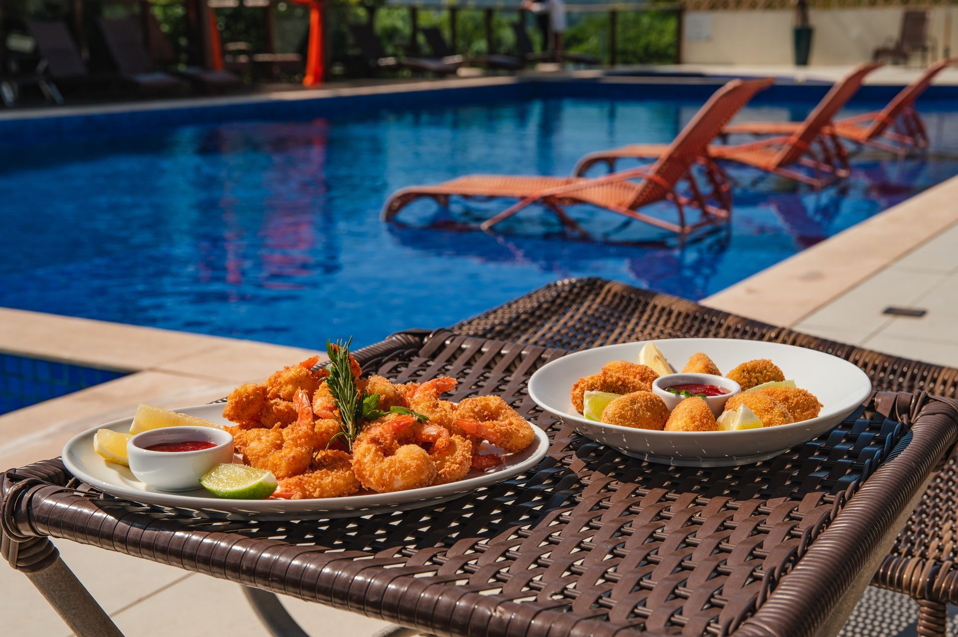 Pratos de comida em uma mesa de vime ao lado de uma piscina azul.
