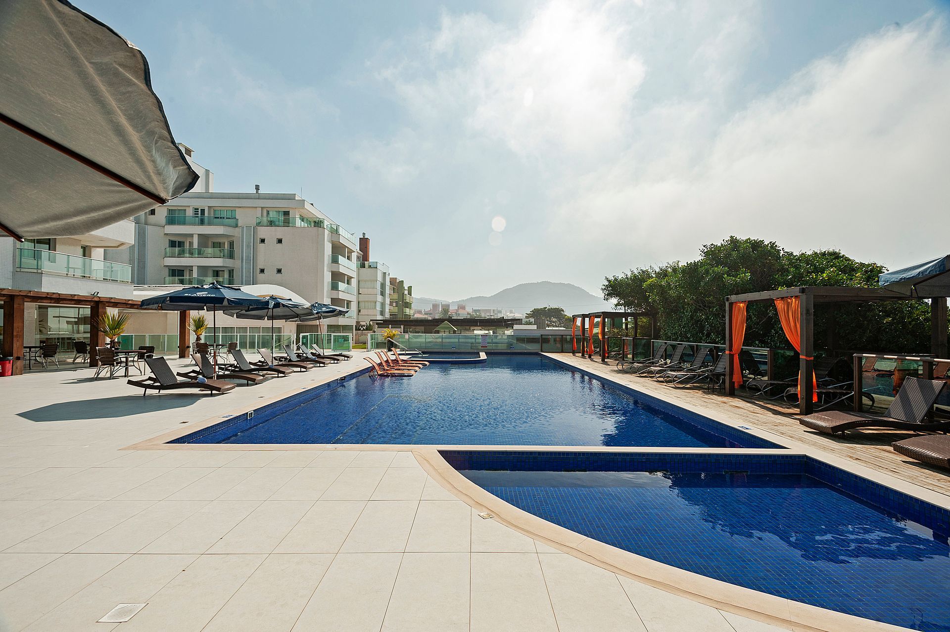 Piscina do resort com água azul, espreguiçadeiras e edifícios do hotel sob um céu nublado.