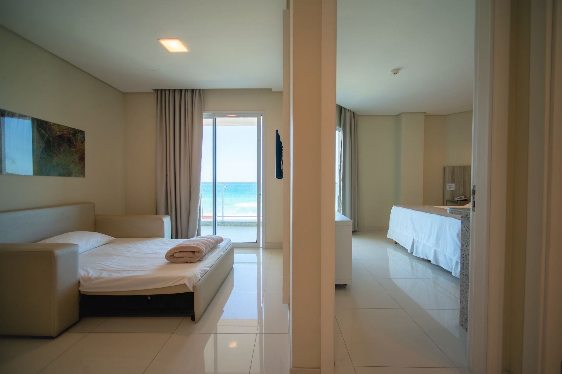 Quarto moderno com cama, armário espelhado e vista para o mar através de portas de varanda.