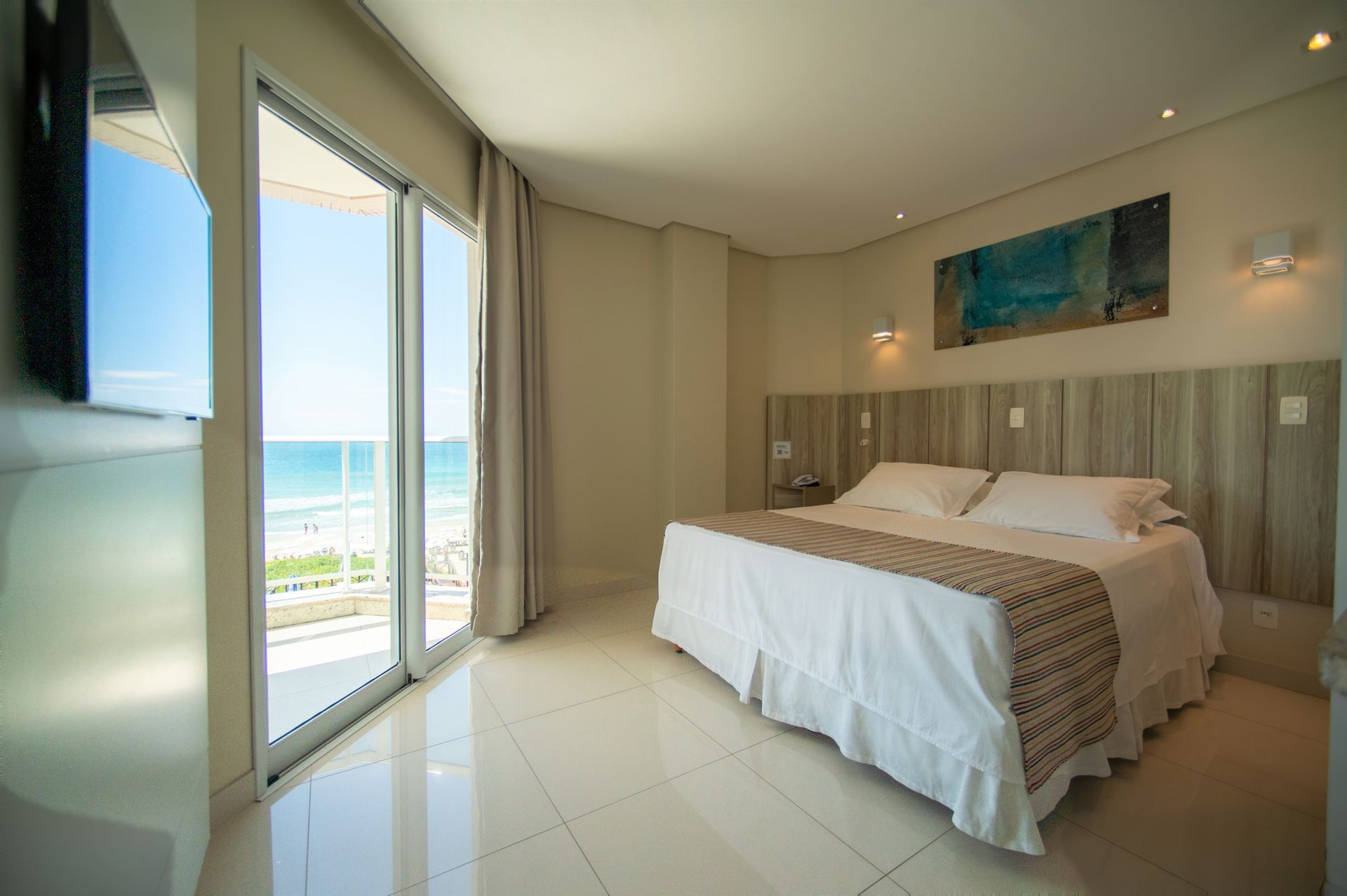 Quarto de hotel luminoso com cama king-size e janelas com vista para o mar.