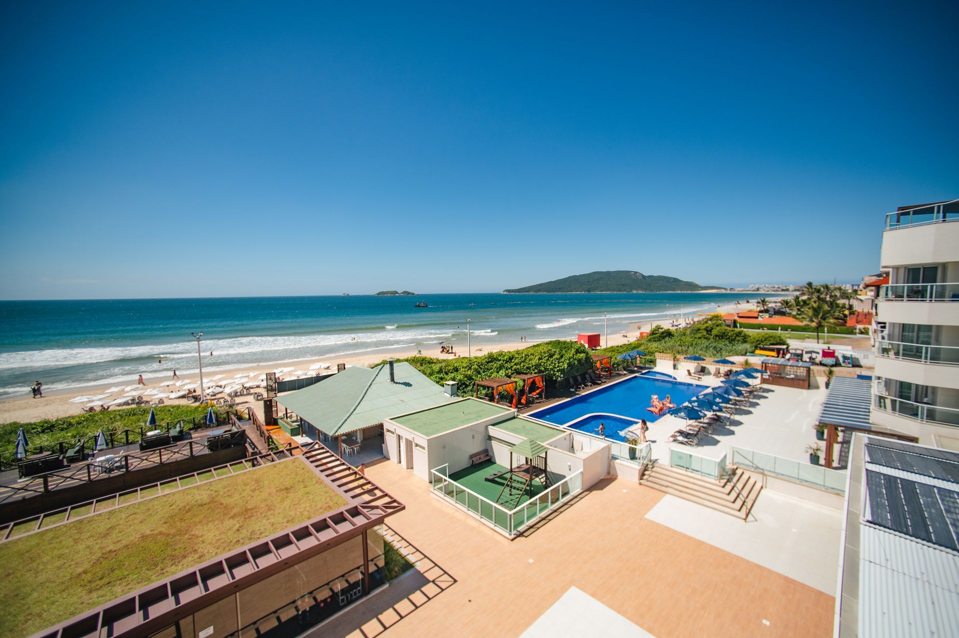 Resort à beira-mar com piscinas, guarda-sóis e uma praia de areia sob um céu azul límpido.