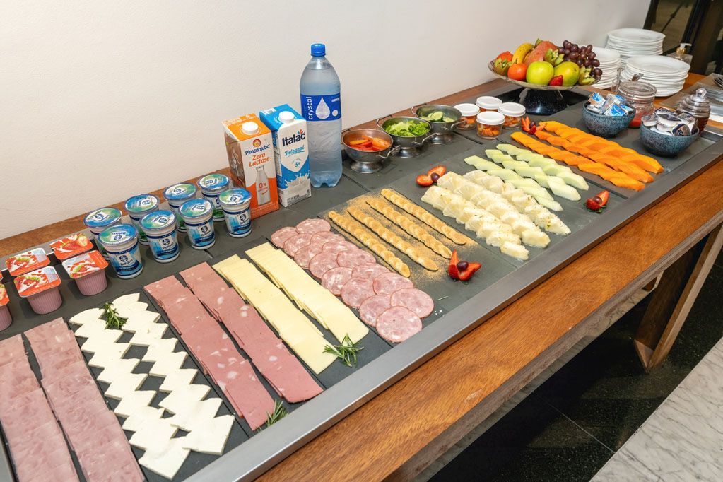 Mesa de buffet com fileiras de sushi, bebidas, frutas e pratos cuidadosamente dispostos.