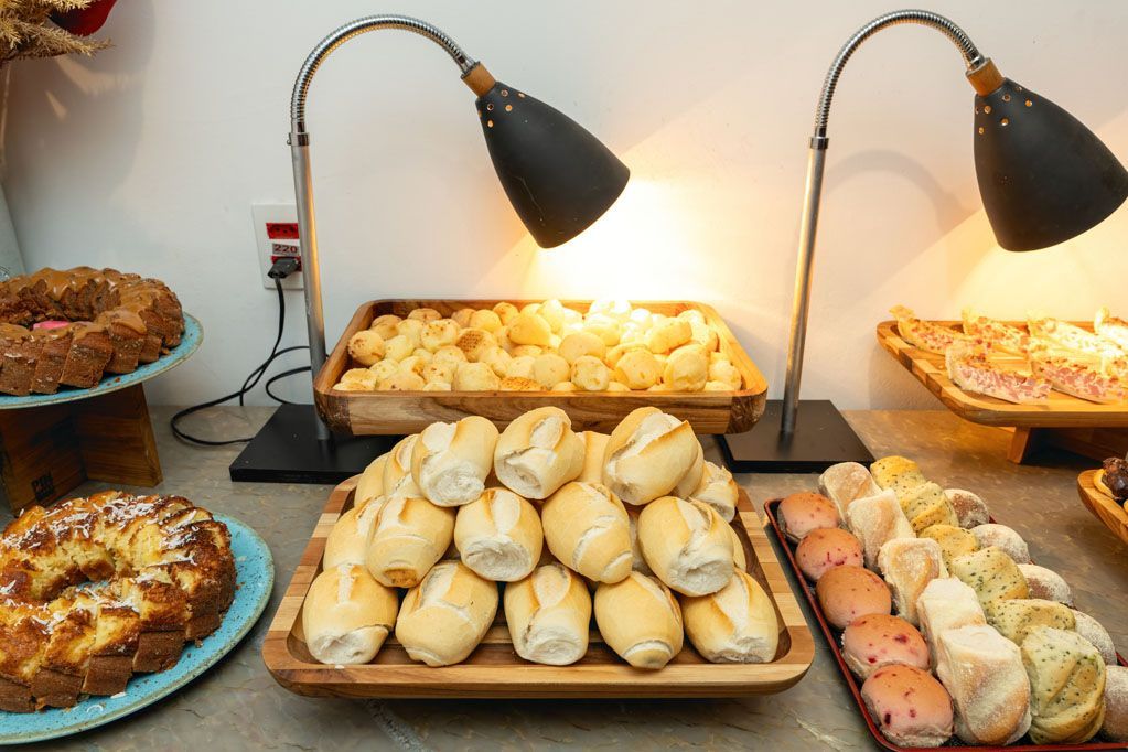 Vitrine de padaria com uma variedade de pães e doces sob duas lâmpadas de aquecimento em um balcão.