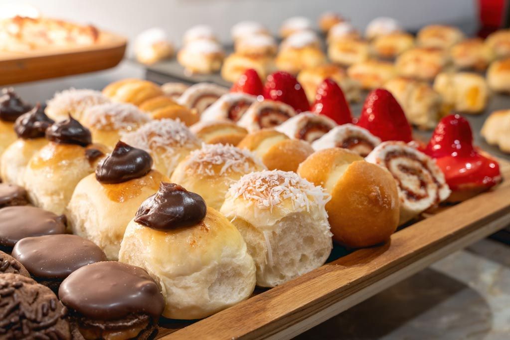Variedade de doces glaceados e confeitados dispostos em bandejas em uma vitrine de padaria.