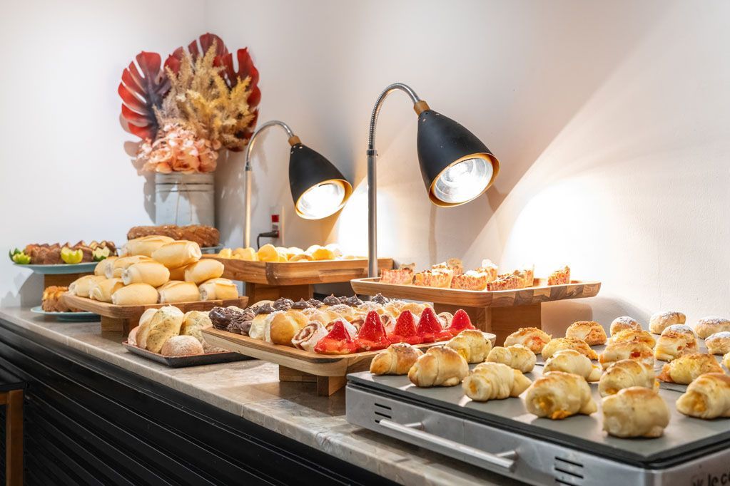 Sobremesas expostas em uma mesa de bufê sob luzes aconchegantes, com doces e tortas de frutas dispostas em fileiras.
