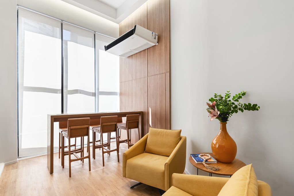 Sala de jantar moderna com mesa de madeira, cadeiras, poltrona amarela e vaso de flores junto a uma janela bem iluminada.