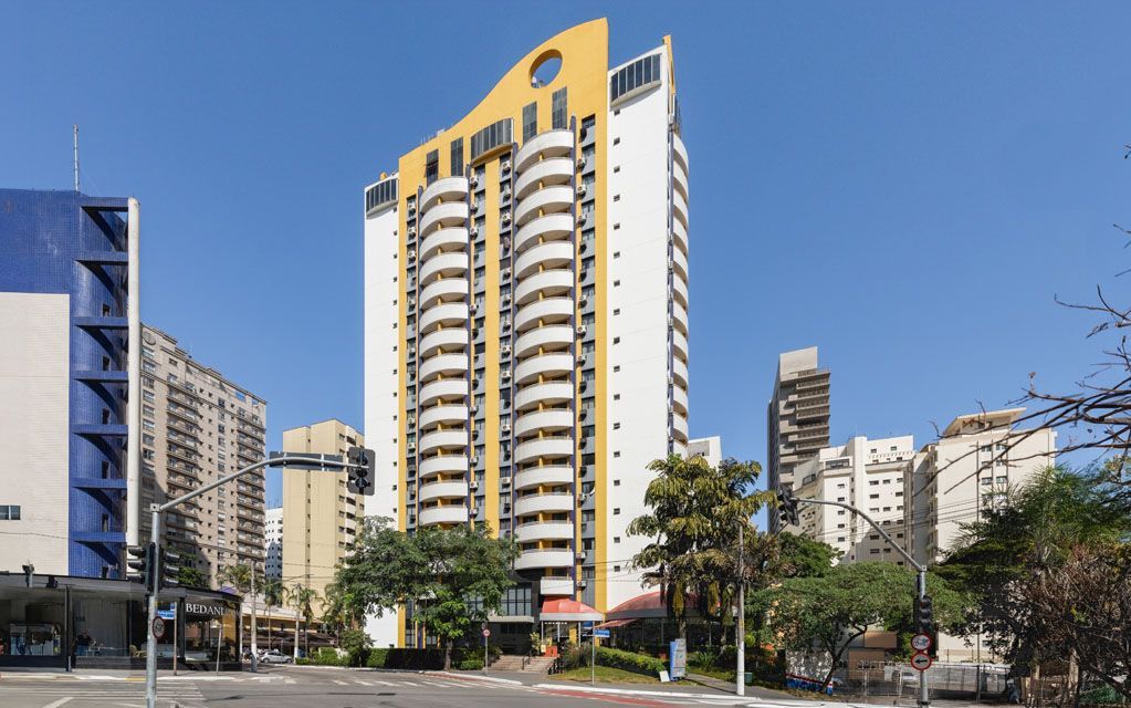 Rua da cidade com um arranha-céu alto amarelo e branco sob um céu azul claro.